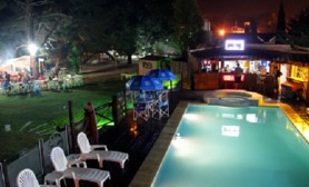 Nuestro Complrjo por las noches, bar con pantalla gigante vista de solarium y piscina title=